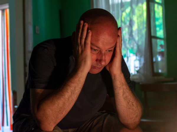 Depressed man sitting head in hands on the chair in the dark room with low light environment