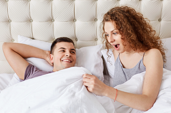 Husband and wife in bed. Wife looking excited after husband ingests an Erectimus instant erection pill.